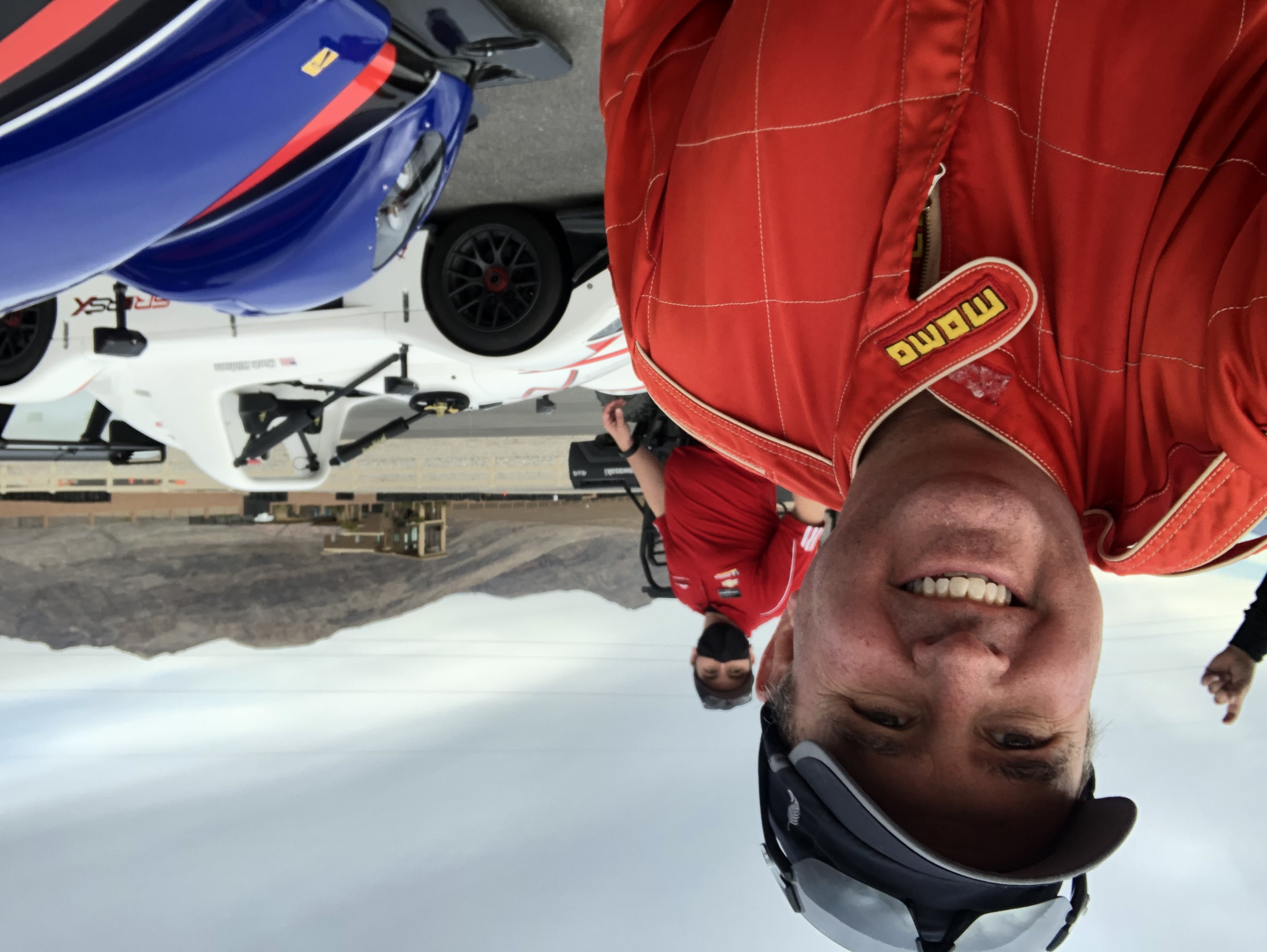 Jeff smiling in a red racing suit beside race cars